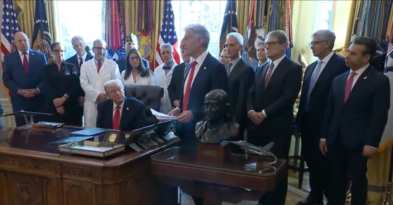 President Donald Trump at his desk in the Oval Office, surrounded by officials, at the signing of the executive order on cannabis rescheduling